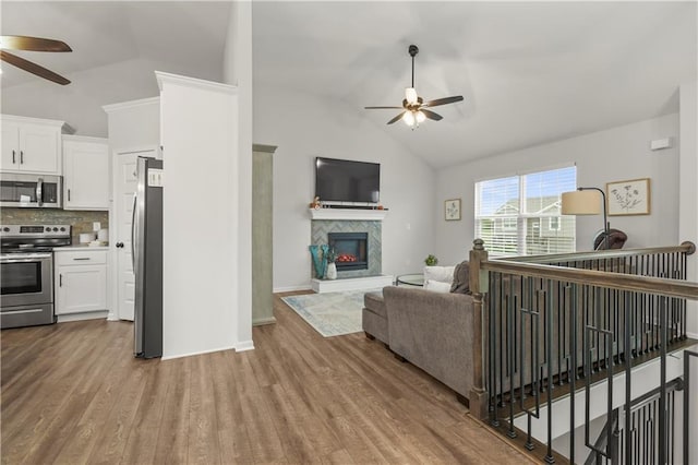 living area with a fireplace, lofted ceiling, a ceiling fan, and wood finished floors