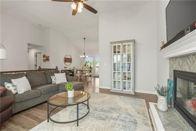 living area with baseboards, ceiling fan with notable chandelier, high vaulted ceiling, wood finished floors, and a fireplace