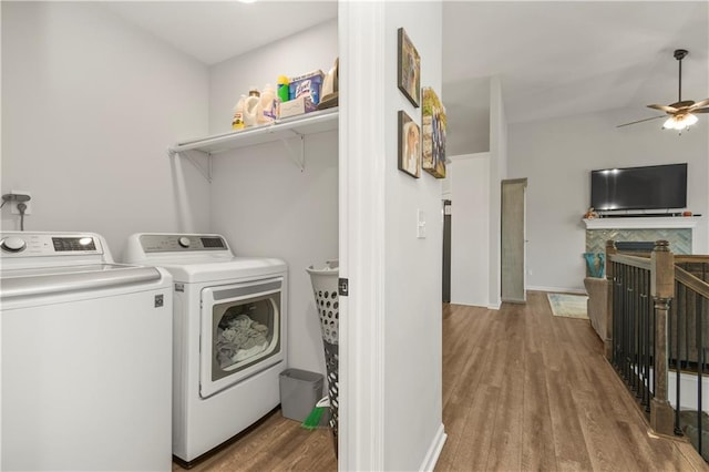 clothes washing area featuring wood finished floors, laundry area, washer and dryer, ceiling fan, and a tile fireplace
