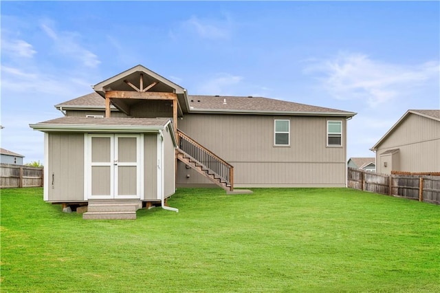back of house featuring stairway, a fenced backyard, and a yard