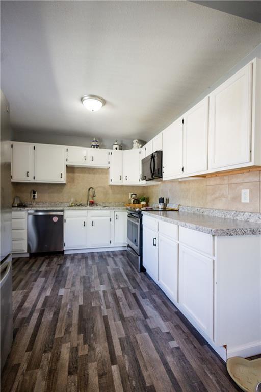 kitchen with dark wood-style floors, stainless steel appliances, a sink, tasteful backsplash, and white cabinetry