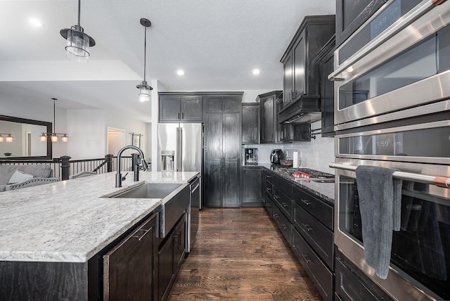 kitchen with dark wood finished floors, appliances with stainless steel finishes, light stone countertops, and a sink