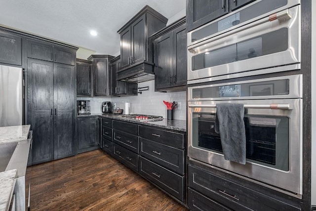 kitchen featuring dark cabinets, appliances with stainless steel finishes, and light stone counters