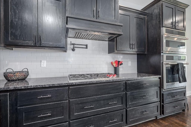 kitchen featuring decorative backsplash, dark stone counters, appliances with stainless steel finishes, and dark wood-style flooring