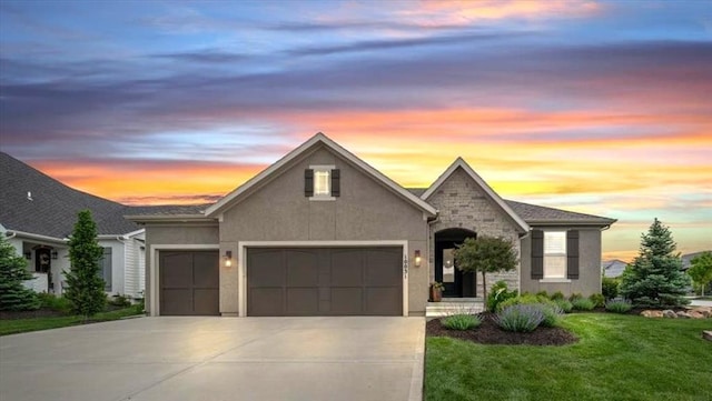 view of front of property featuring an attached garage, driveway, a yard, stucco siding, and stone siding