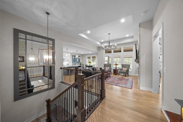 corridor with an upstairs landing, a chandelier, wood finished floors, baseboards, and recessed lighting
