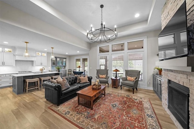 living area featuring a fireplace, a tray ceiling, a chandelier, recessed lighting, and light wood-style floors