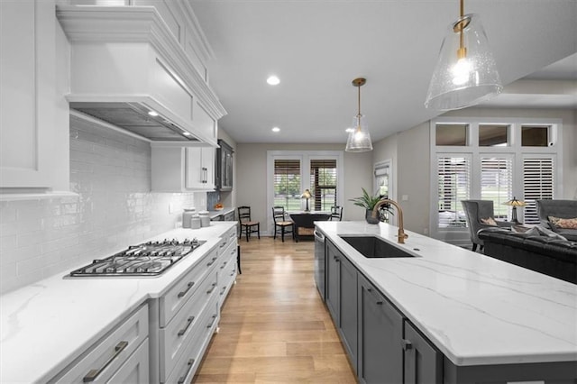 kitchen with a sink, stainless steel gas stovetop, white cabinetry, light wood-type flooring, and recessed lighting