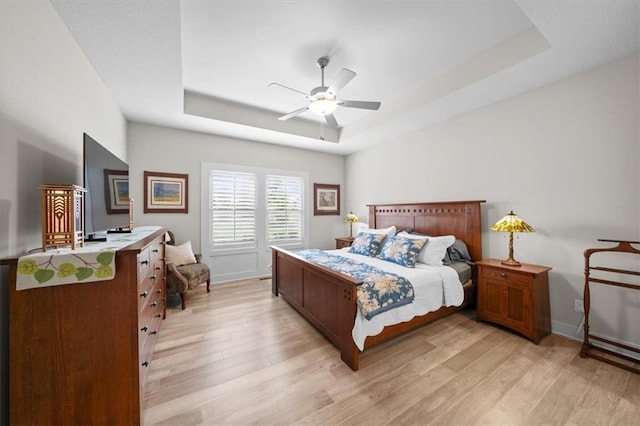bedroom with a raised ceiling, light wood-type flooring, and baseboards