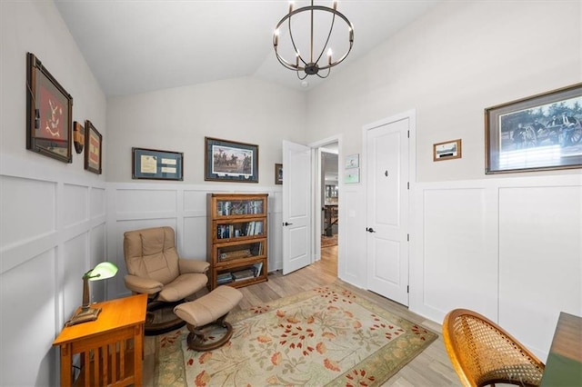 living area with light wood finished floors, a chandelier, a decorative wall, a wainscoted wall, and vaulted ceiling