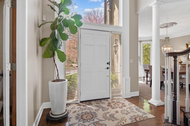 entryway with crown molding, dark wood finished floors, baseboards, an inviting chandelier, and ornate columns