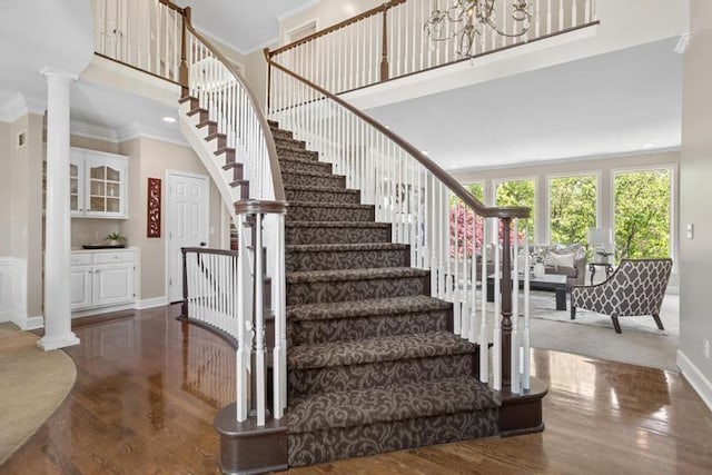 stairway with ornamental molding, decorative columns, wood finished floors, baseboards, and a high ceiling