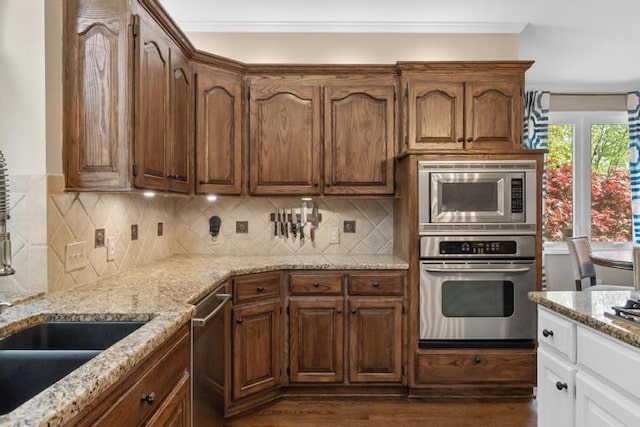 kitchen featuring appliances with stainless steel finishes, light stone counters, ornamental molding, decorative backsplash, and dark wood-style floors