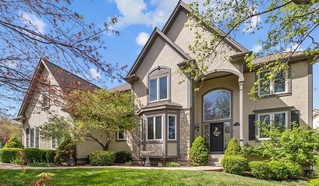 view of front facade featuring a front lawn, stone siding, and stucco siding