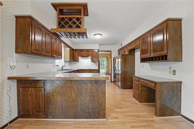 10503 W 50th Ter, Shawnee, KS 66203 - kitchen featuring wallpapered walls, light wood finished floors, a peninsula, a sink, and baseboards