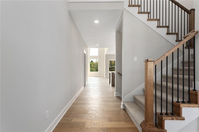 hall featuring recessed lighting, hardwood / wood-style floors, baseboards, and stairway