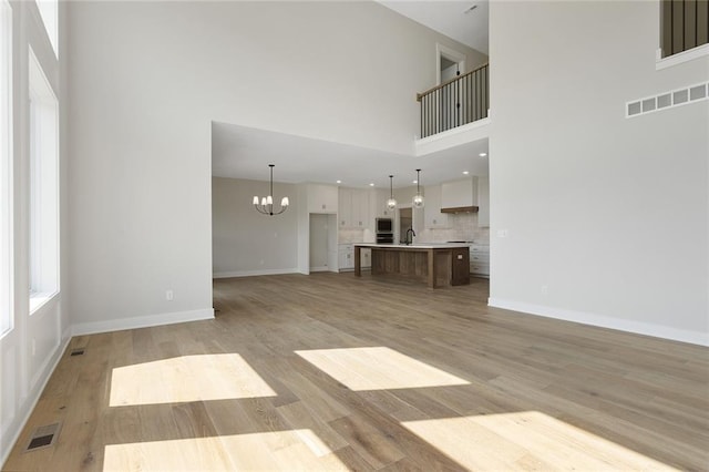unfurnished living room featuring light wood-type flooring, a high ceiling, a notable chandelier, and visible vents