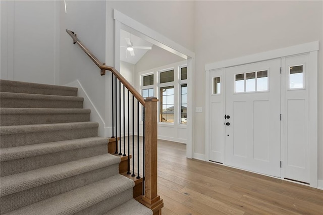 foyer featuring a high ceiling, light wood-style floors, baseboards, stairs, and ceiling fan