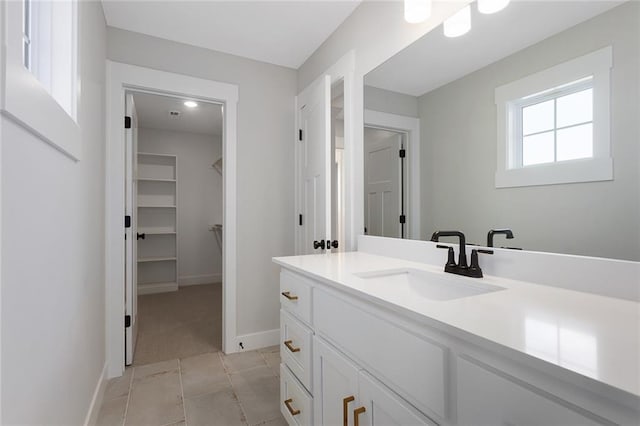 bathroom with a walk in closet, baseboards, tile patterned floors, and vanity