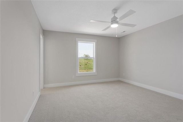 spare room featuring light carpet, a ceiling fan, and baseboards