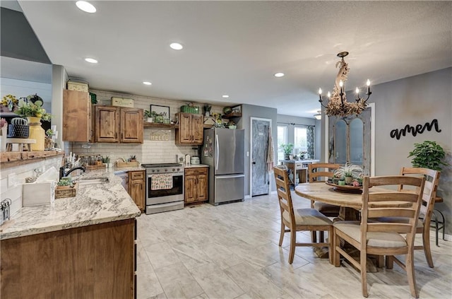 kitchen with an inviting chandelier, light stone counters, brown cabinetry, stainless steel appliances, and tasteful backsplash