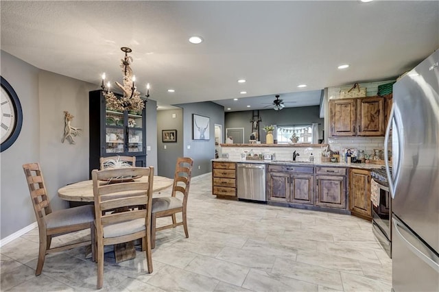 kitchen with decorative backsplash, baseboards, a sink, ceiling fan with notable chandelier, and stainless steel appliances