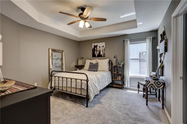 bedroom featuring baseboards, a tray ceiling, ceiling fan, and carpet