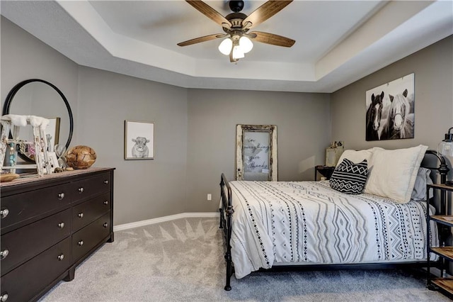 bedroom with a raised ceiling, baseboards, ceiling fan, and light colored carpet