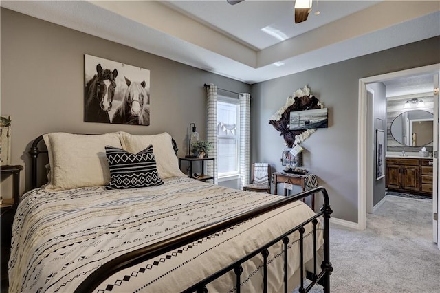 bedroom featuring ceiling fan, light colored carpet, baseboards, ensuite bathroom, and a tray ceiling