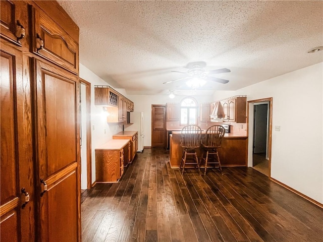 628 S Clay St, Nevada, MO 64772 - kitchen featuring ceiling fan, a kitchen breakfast bar, brown cabinets, a peninsula, and dark wood-style floors