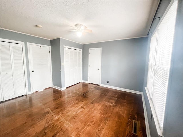 628 S Clay St, Nevada, MO 64772 - unfurnished bedroom featuring baseboards, ornamental molding, two closets, and wood finished floors