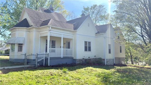 628 S Clay St, Nevada, MO 64772 - view of home's exterior featuring covered porch, a chimney, roof with shingles, fence, and a yard