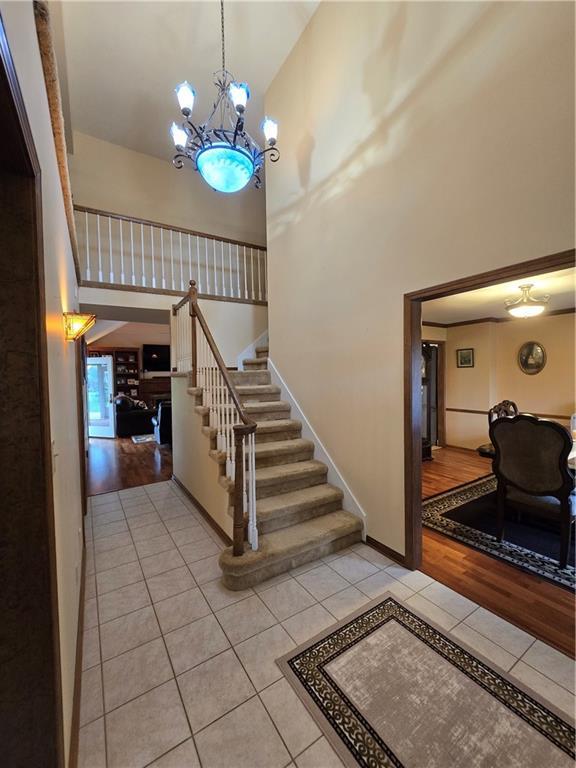 1502 Hillcrest Ct, Atchison, KS 66002 - staircase with tile patterned flooring, high vaulted ceiling, a chandelier, and baseboards