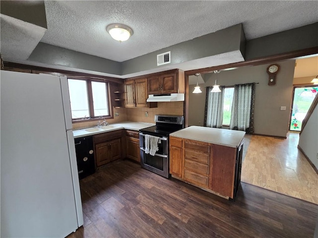 kitchen with under cabinet range hood, range with two ovens, visible vents, a peninsula, and freestanding refrigerator