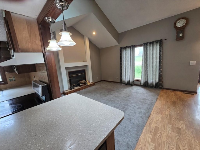 kitchen featuring a glass covered fireplace, baseboards, vaulted ceiling, pendant lighting, and wood finished floors