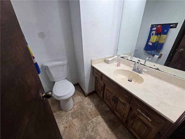 bathroom featuring toilet, stone finish floor, vanity, and baseboards