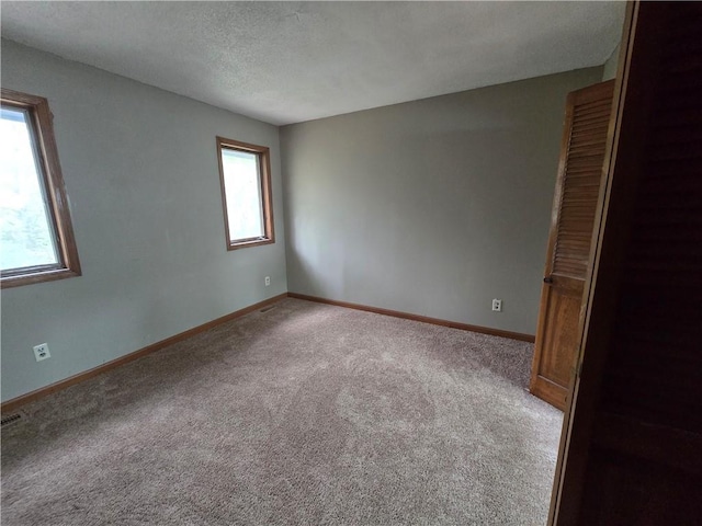 carpeted spare room featuring baseboards and a textured ceiling
