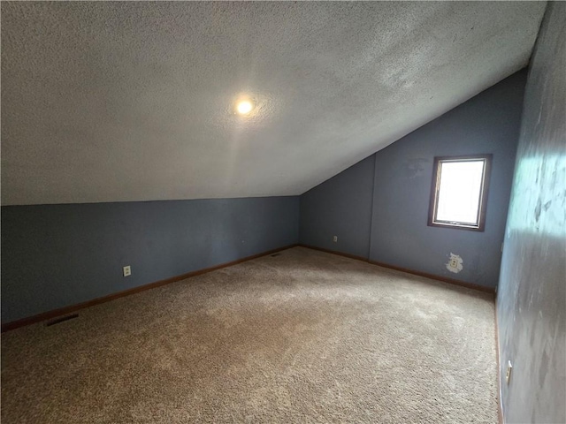 additional living space featuring carpet floors, visible vents, baseboards, a textured ceiling, and lofted ceiling
