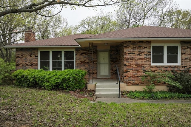 single story home with roof with shingles, a chimney, a front yard, and brick siding