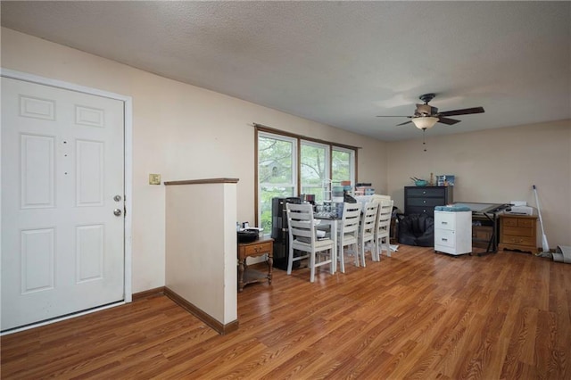 office featuring a textured ceiling, ceiling fan, baseboards, and light wood-style floors