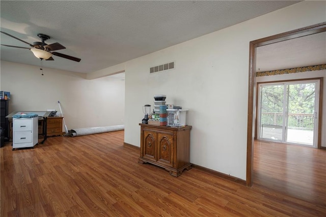 office area featuring a ceiling fan, visible vents, wood finished floors, and baseboards