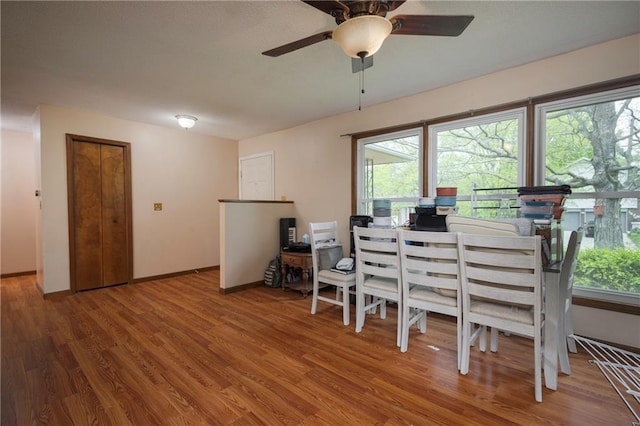 dining room featuring wood finished floors, a healthy amount of sunlight, a ceiling fan, and baseboards