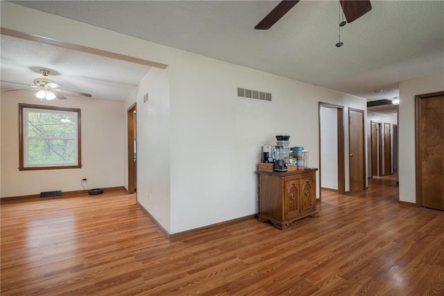 hall featuring a textured ceiling, visible vents, and light wood-style flooring