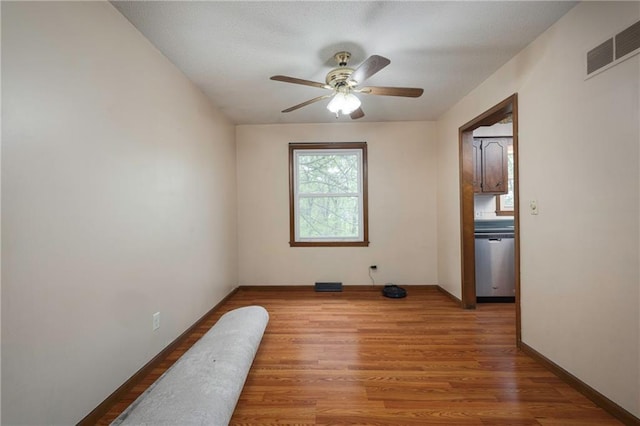 unfurnished room with visible vents, light wood-type flooring, a ceiling fan, and baseboards