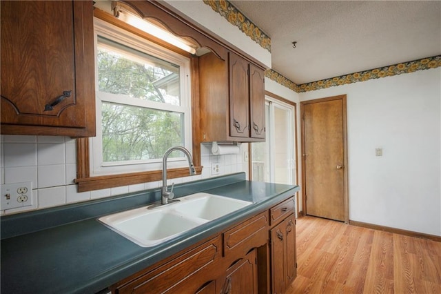 kitchen featuring tasteful backsplash, dark countertops, light wood finished floors, and a sink