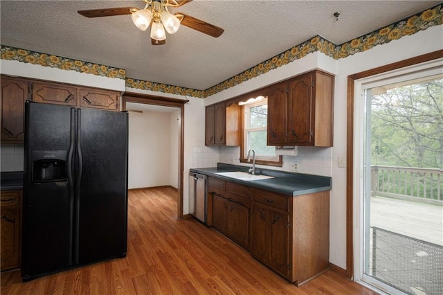 kitchen featuring a sink, black refrigerator with ice dispenser, light wood-type flooring, dark countertops, and dishwasher