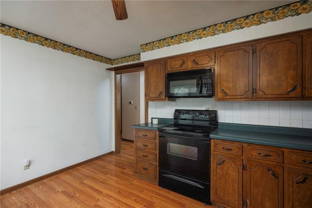 kitchen featuring black appliances, dark countertops, light wood finished floors, and backsplash