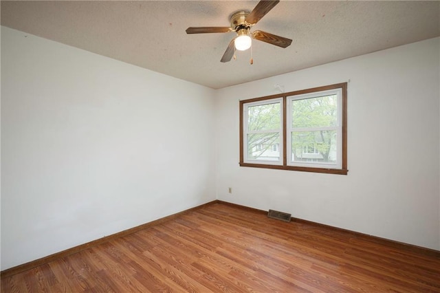 unfurnished room with a textured ceiling, light wood-style flooring, visible vents, ceiling fan, and baseboards