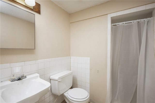 full bathroom featuring a shower with curtain, tile walls, a sink, toilet, and wainscoting