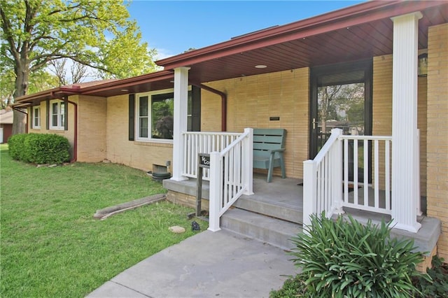 view of exterior entry featuring a lawn, brick siding, and a porch